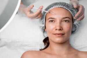 Dermatologista aplica toxina botulínica na testa de uma paciente em ambiente clínico, com técnica e cuidado.